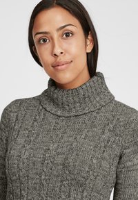 Szürke, cable-knit garbó pulóver, amely texturált mintázattal és vastag bordás gallérral rendelkezik, kiemelve a kényelmes, meleg megjelenést.