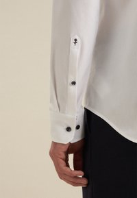 Witte overhemd met lange mouwen, voorzien van zwarte knopen en een geborduurde bloemendetail op de manchet. Glad materiaal met een getailleerde pasvorm.
