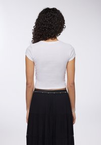 Crop top bianco a coste con maniche corte, abbinato a una gonna maxi nera a balze con dettagli in pizzo e una cintura sottile.