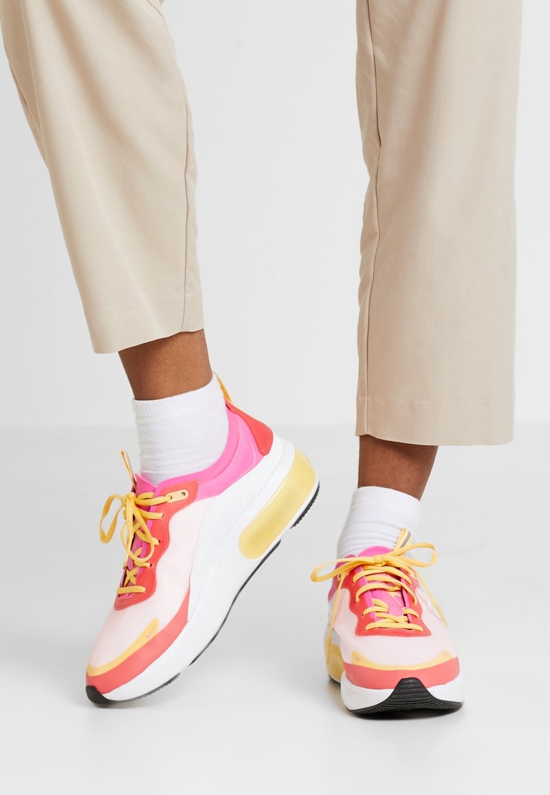 Sneakers feature a pink, white, and yellow color scheme with mesh and synthetic materials. Thick cushioned sole with a black rubber outsole.