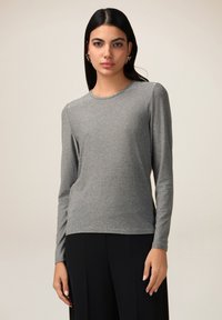 Cămașă gri cu mâneci lungi, dintr-un tricot moale și texturat, cu guler rotund. Asortată cu pantaloni negri, cu un fit lejer. Fără modele sau accente vizibile.
