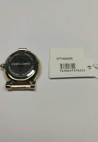 Ferragamo watch with a round stainless steel case, black dial, and a clasp. Accompanied by a tag with barcode and product code.