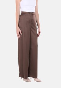 Pantaloni marroni in raso a gamba larga con finitura liscia, vita alta e davanti pulito, abbinati a tacchi a punta color nudo.