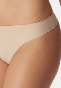 Perizoma beige realizzato in un tessuto liscio e elasticizzato. Presenta un cinturino sottile e una copertura minima con bordi senza cuciture.