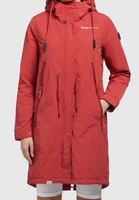 Red long waterproof jacket with a hood, adjustable drawstrings, front zip pockets, and logo accents. Smooth texture, relaxed fit.