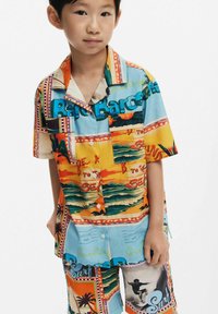 Ryškiai spalvota trumpomis rankovėmis marškinėlių ir šortų komplektas su tropinio atviruko spauda, vaizduojančia palmės medžius ir banglenčių scenas.