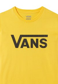 Camiseta de algodón amarilla con un destacado logo negro de "VANS" en una fuente audaz, con un corte clásico y un cuello redondo. Textura suave.