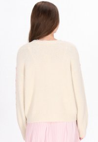 Crème-kleurige gebreide sweater met een relaxte pasvorm, voorzien van gestructureerde roze pompons langs de mouwen en een geribbelde onderrand.