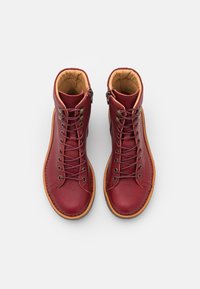 Botas de tobillo de cuero rojo con textura suave, punta redonda, cordones verde oliva y plantillas de color marrón claro. Cierre lateral con cremallera para un fácil acceso.