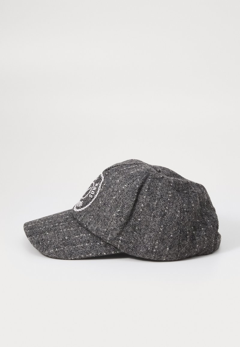 Gorra de patrón espiga en gris con visera estructurada, que presenta un parche bordado circular en la parte frontal. La textura de la tela parece tejida.