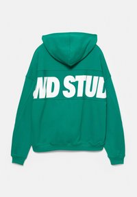 Grøn hættebluse med en stor hvid "AND STUD" tekst på tværs af den øverste del af ryggen. Blødt stof, afslappet pasform med ribbede manchetter og kant.