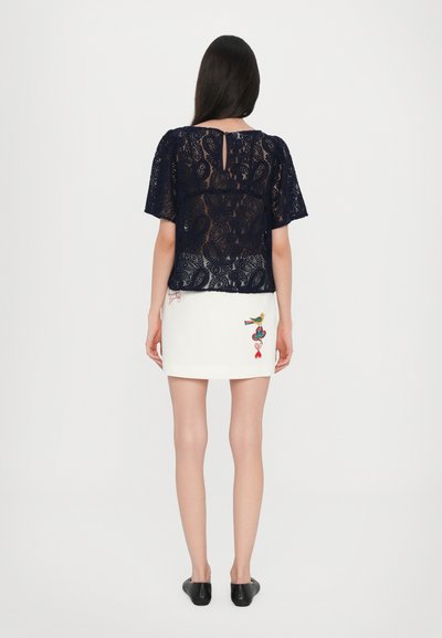 Navy lace top with short sleeves features intricate floral patterns, paired with a white mini skirt adorned with colorful embroidery designs.