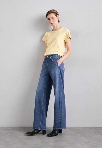 Lys gul kortermet t-skjorte kombinert med vide blå denimjeans. Antrekket kompletteres med svarte hælankelstøvler.