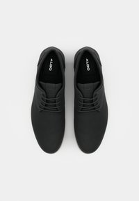 Zapatos negros con cordones, con parte superior de tela suave, punta redonda y suela color crema. Logotipo visible en la plantilla negra.