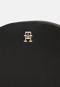 Pochette nera in pelle con zip, con dettagli del logo in tono oro nella parte superiore, caratterizzata da una trama liscia e una forma arrotondata.