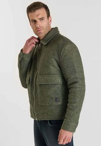 Chaqueta de mezcla de lana verde oliva con cierre de cremallera, cuello desplegable, dos bolsillos frontales y un pequeño parche con el logo en el lado izquierdo.