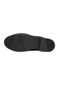 Suela de zapato de goma negra con patrones texturizados, ranuras definidas para tracción y un acento rectangular cerca del talón. Marca de talla: 39.