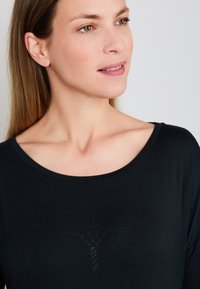 Czarna koszulka z szerokim dekoltem i długimi rękawami, z ozdobnym wzorem z cyrkonii przedstawiającym liść na piersi.