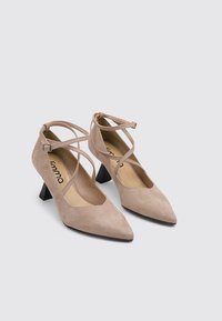 Zapatos de tacón alto de ante beige con punta puntiaguda y tacón ancho. Cuentan con tiras cruzadas en el tobillo y un forro interior suave.