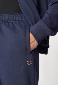 Φούτερ σκούρου μπλε με φερμουάρ μπροστά. Μαλακό, υφασμένο ύφασμα. Διαθέτει τσέπη και κεντημένο λογότυπο στα παντελόνια. Άνετη εφαρμογή.