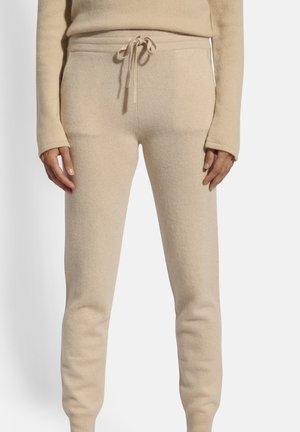 Jogging con tessuto beige e morbido, con vita regolabile a coulisse, polsini a coste e texture liscia, caratterizzati da un design aderente e senza motivi visibili.