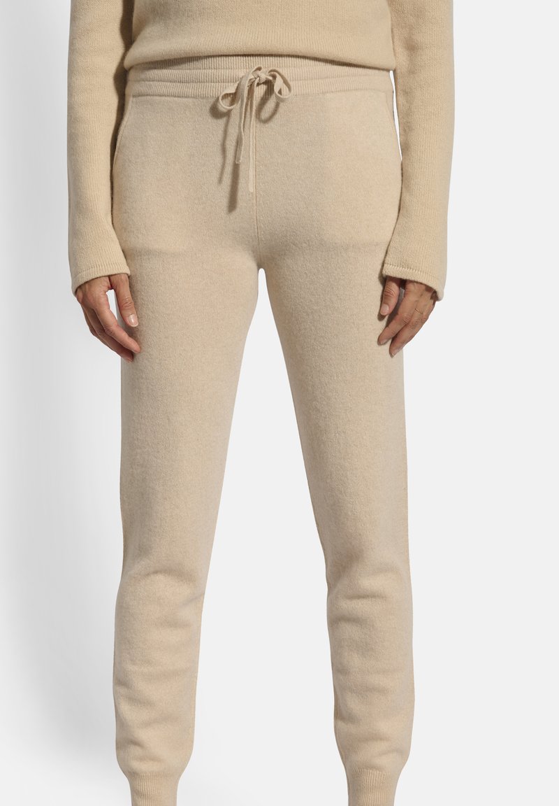 Beige, weiche Stoff-Jogginghosen mit elastischem Bund, gerippten Bündchen und glatter Textur, die ein tailliertes Design ohne sichtbare Muster aufweisen.