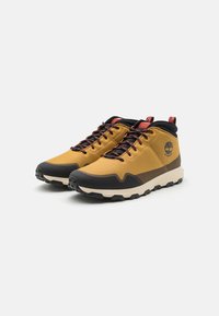 Zapatos de senderismo amarillos con parte superior de malla texturizada, tapa de goma negra en la punta y acentos rojos contrastantes. Suela gruesa y resistente diseñada para ofrecer tracción.