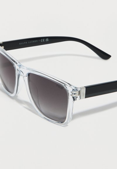 Διαφανή ορθογώνια γυαλιά ηλίου με φακούς μαύρου διαβαθμισμένου χρώματος, διαφανή πλαίσια και μαύρους βραχίονες με ασημένιες μεντεσέδες.