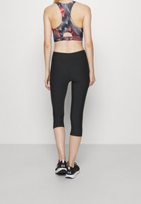 Leggings capri neri abbinati a un reggiseno sportivo geometrico multicolore con un design a schiena scoperta. Entrambi gli articoli sono progettati per l'abbigliamento sportivo.