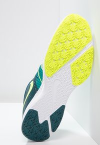 Zapatilla con parte superior texturizada en color verde azulado y una suela blanca con un agarre con patrón. Detalles en amarillo fluorescente a lo largo de los lados.