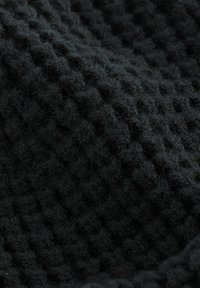 Svart texturerad tyg med rutmönster, med en mjuk, fluffig yta. Materialet verkar tjockt och varmt.