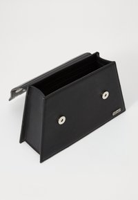 Portefeuille rectangulaire noir avec rabat, doté de deux fermetures à pression métalliques et d'un logo embossé sur le côté, reposant sur un fond blanc.