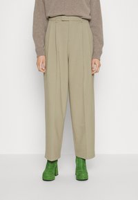 Hoog getailleerde, geplooide broek in licht khaki stof, voorzien van een ceintuur in de taille en een wijde pijpdesign, gecombineerd met groene suède platformlaarzen.