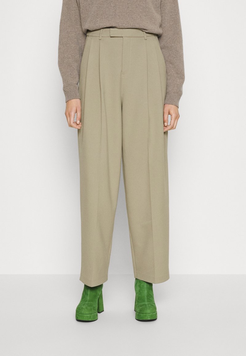 Hoog getailleerde, geplooide broek in licht khaki stof, voorzien van een ceintuur in de taille en een wijde pijpdesign, gecombineerd met groene suède platformlaarzen.