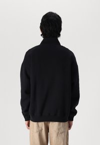 Sweatshirt noir surdimensionné avec un col haut et un ourlet côtelé. Texture douce, avec des épaules tombantes et sans logos ni accents visibles.