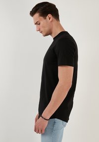 Černé tričko s krátkým rukávem vyrobené z bavlny, s klasickým designem kulatého výstřihu. Nosené s světle modrými džíny, které zvýrazňují fitted siluetu.