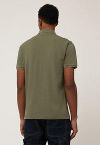 Polo de color oliva hecho de algodón, con una textura suave, mangas cortas y un cuello clásico; la vista trasera muestra un diseño sencillo.