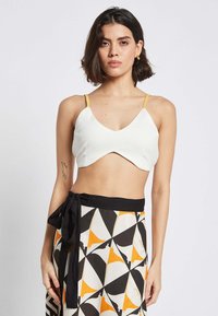 White cropped top with a V-neck and yellow straps, paired with a skirt featuring a geometric black, white, and orange pattern.