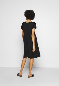 Robe noire à manches courtes avec une coupe ample et un design à volants, confectionnée dans un tissu doux. Elle présente un col rond et un ourlet mi-long.
