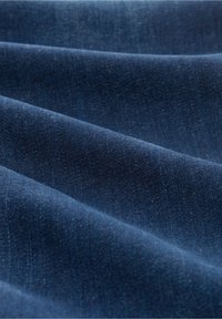 Tejido de mezclilla azul oscuro con una textura suave, que presenta variaciones sutiles en el tono y un tenue patrón de tejido. Se pueden ver pliegues horizontales.