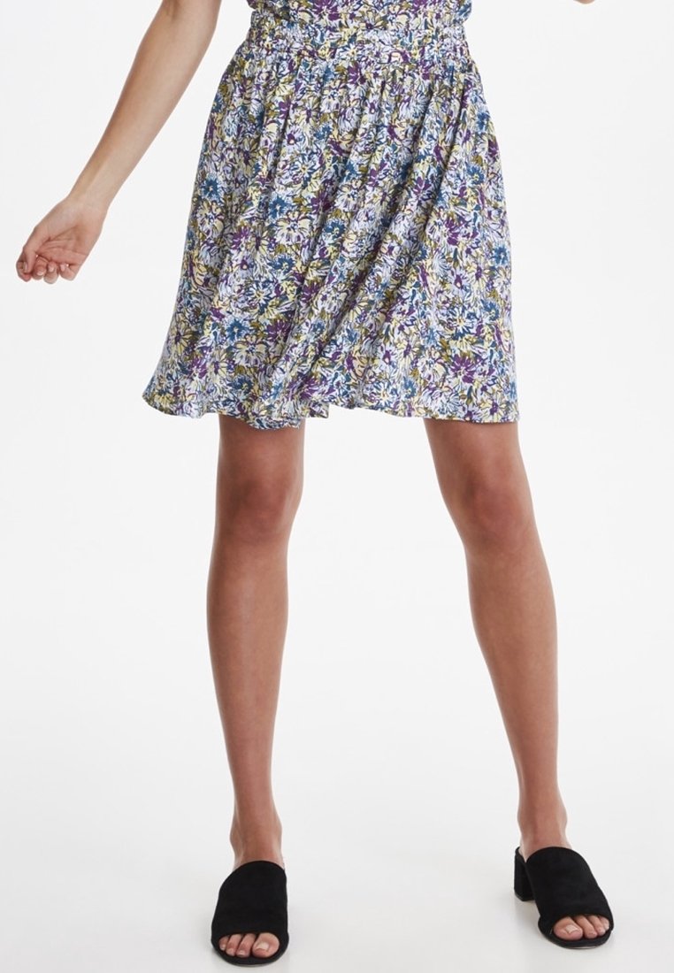 Gonna floreale con vita aderente, caratterizzata da un mix di motivi viola, blu e gialli. Leggera, sopra il ginocchio, abbinata a scarpe slip-on nere.