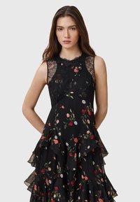 Black dress with floral patterns, sleeveless design, lace neckline, and layered ruffle hem. Made of lightweight fabric with a soft texture.