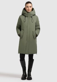 Olivegrüner gepolsterter Mantel mit hohem Kragen und Kordelzugkapuze. Verfügt über einen verdeckten Frontreißverschluss, seitliche Taschen und einen geraden Schnitt. Schwarze kniehohe Stiefel.