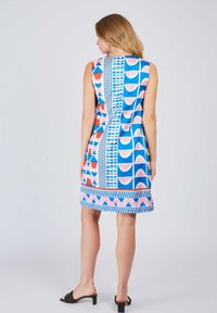 Ärmelloses, knielanges Kleid mit blauem Hintergrund und geometrischen Mustern in Pink und Orange sowie einem dekorativen Saum. Glatte Stofftextur.