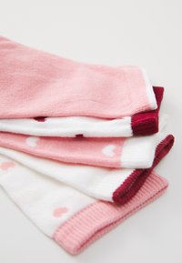 Quatre paires de chaussettes dans des nuances variées de rose et blanc, dotées de motifs en forme de cœur et de côtes contrastantes en rose foncé et bourgogne.