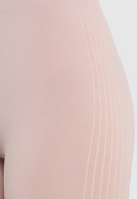 Zbliżenie na bladoróżowe legginsy z wysokim stanem, ozdobione teksturowanymi pionowymi paskami po bokach.