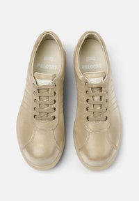 Zapatillas de cuero beige claro con punteras redondas, diseño de cordones de seis ojales y costuras horizontales sutiles en los laterales. Branding "Camper Pelotas" en el interior.