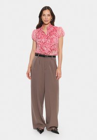Pink floral ruffled blouse with short sleeves, paired with high-waisted brown wide-leg trousers. Black belt and pointed-toe shoes complete the look.