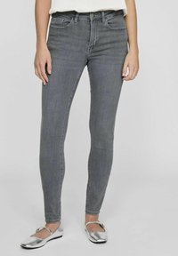Pantalones vaqueros ajustados de denim gris con un diseño ceñido, que presentan una cintura alta, cinco bolsillos y un ligero desgastado. Combinados con zapatos planos plateados.