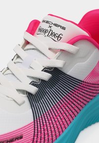 Λευκό αθλητικό παπούτσι με ροζ, μαύρες και μπλε ρίγες, λευκά κορδόνια και λογότυπο "Skechers X Snoop Dogg" στη γλώσσα του παπουτσιού.